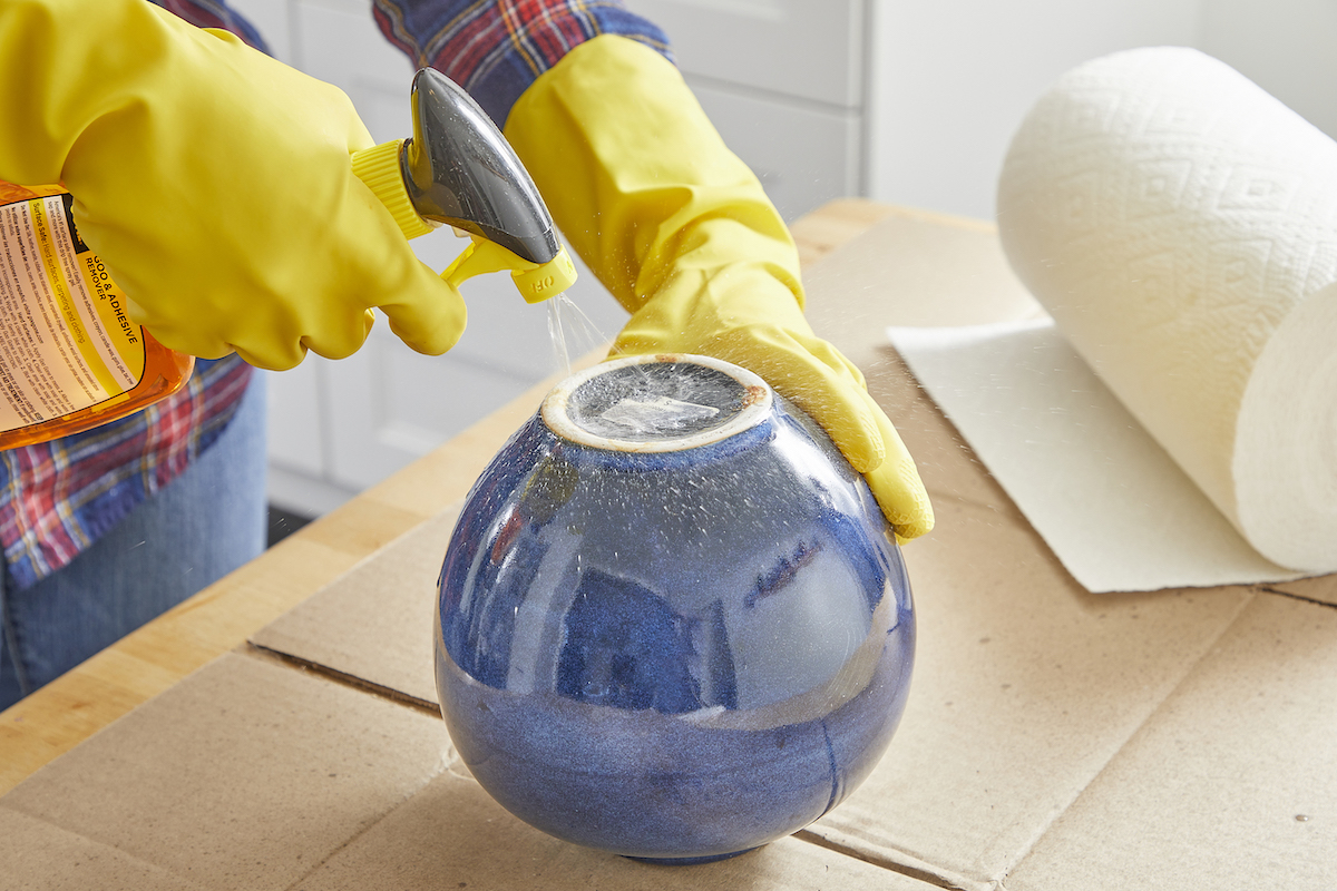 Woman sprays adhesive removal spray on a sticker on the bottom of a jar.