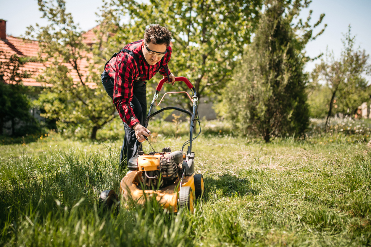 man pulling starter cord on lawn mower in backyard