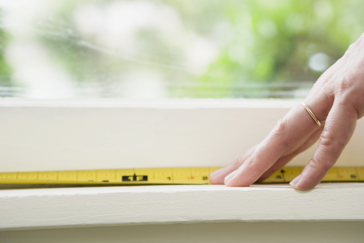 Woman measuring windowsill with yellow tape measure.