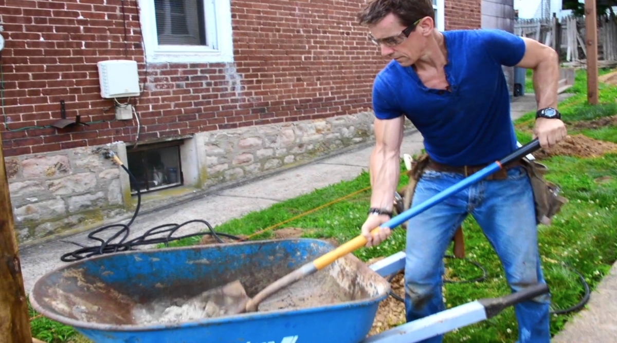 Man mixing concrete in blue wheelbarrow.