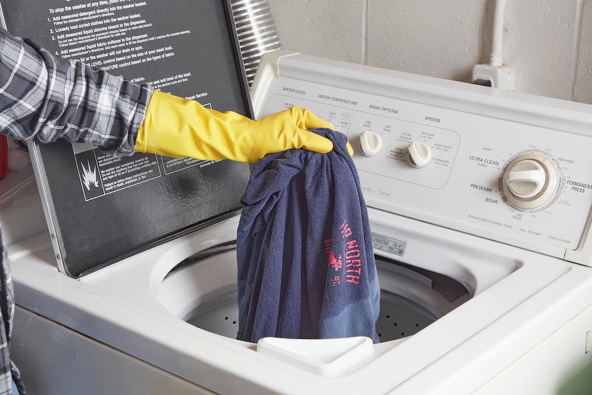 A gloved hand is inserting a wet shirt into the washing machine.