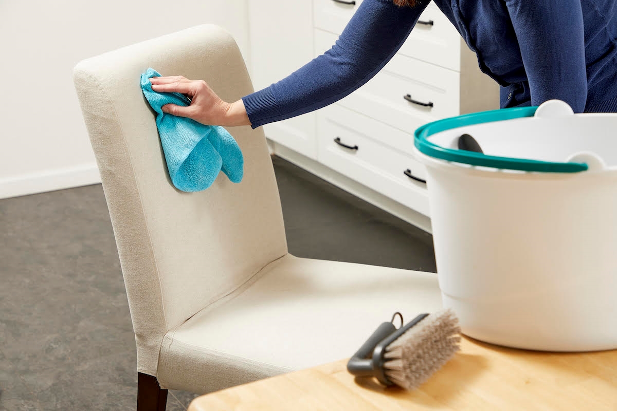 A person is using a microfiber cloth to clean an upholstered chair.