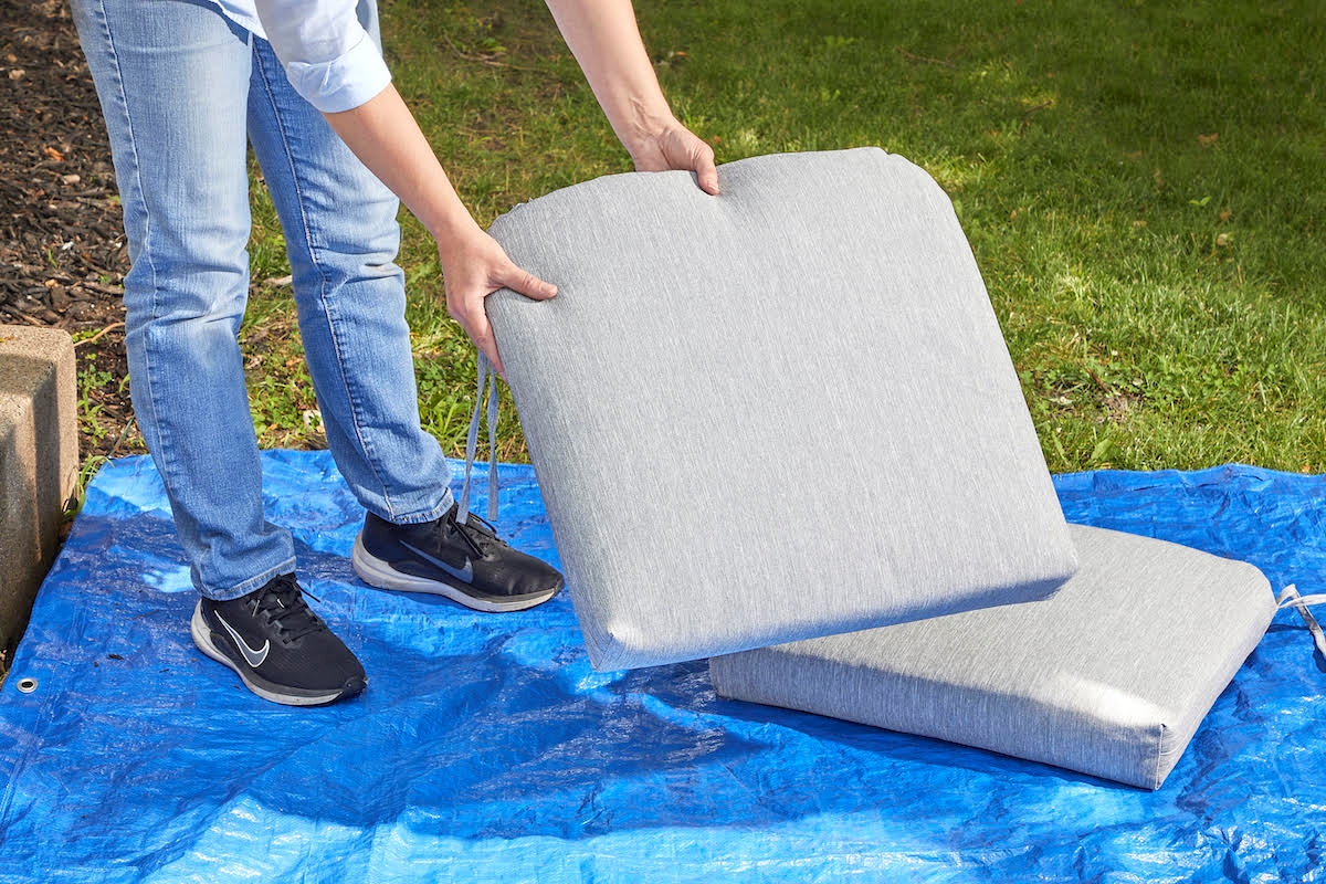 A person is laying clean patio cushions outside on a blue tarp.