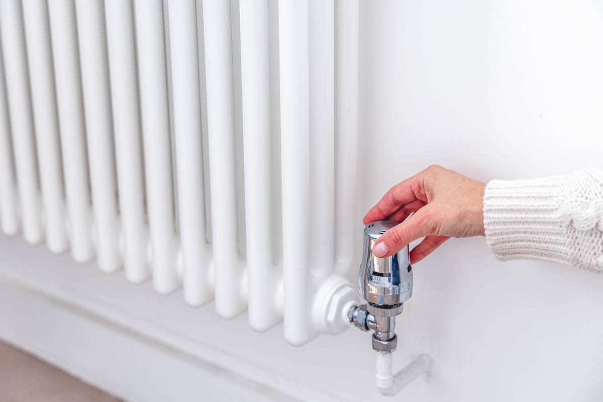 A woman's hand adjusting the thermostat valve on a heating radiator at home.