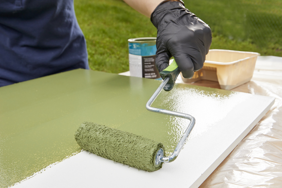 Woman using a roller to paint a piece of white MDF a shade of green.