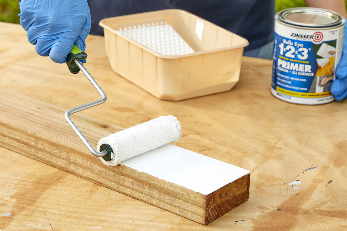 Woman uses small paint roller to prime a 2x4 of pressure treated wood.