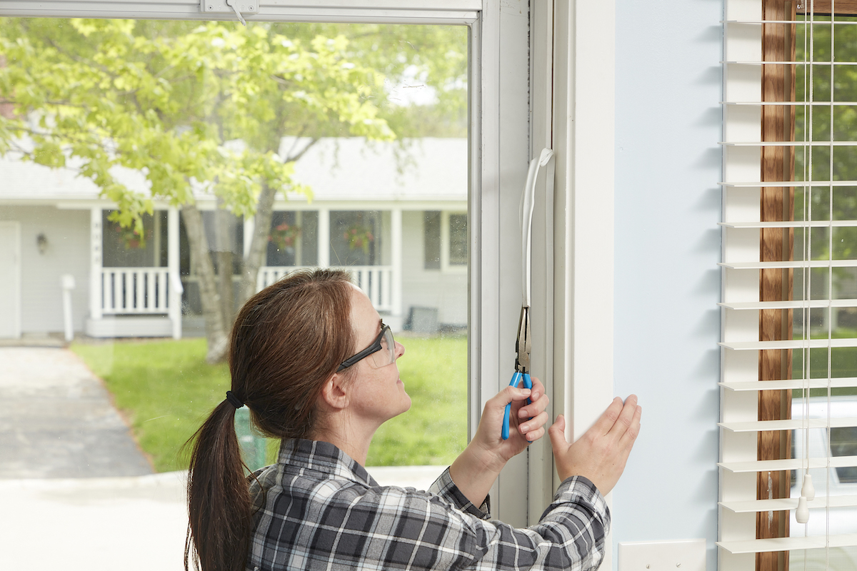 Woman uses needle-nose pliers to pull weather stripping off from around a door.