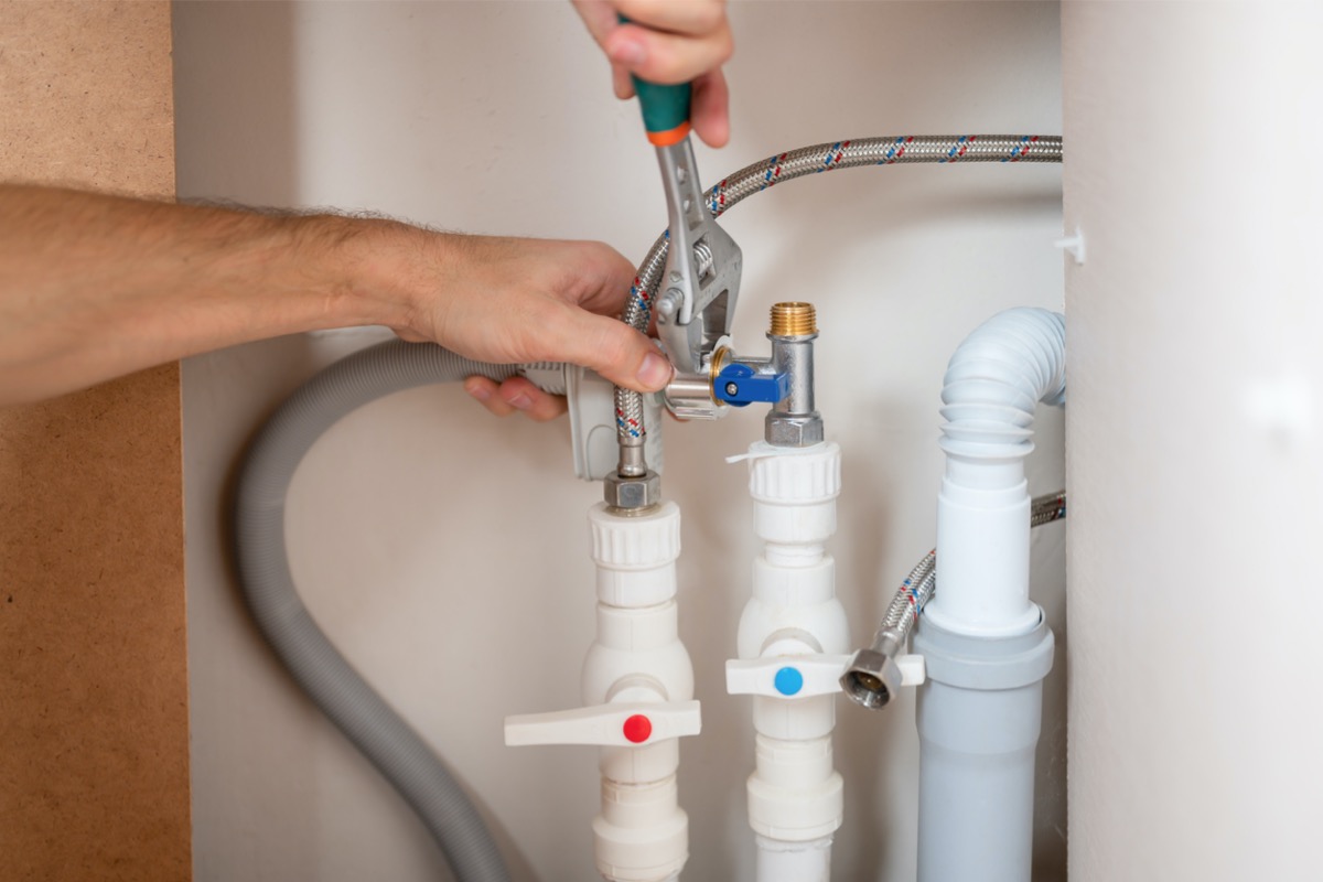 Man uses wrench on piping under kitchen sink.