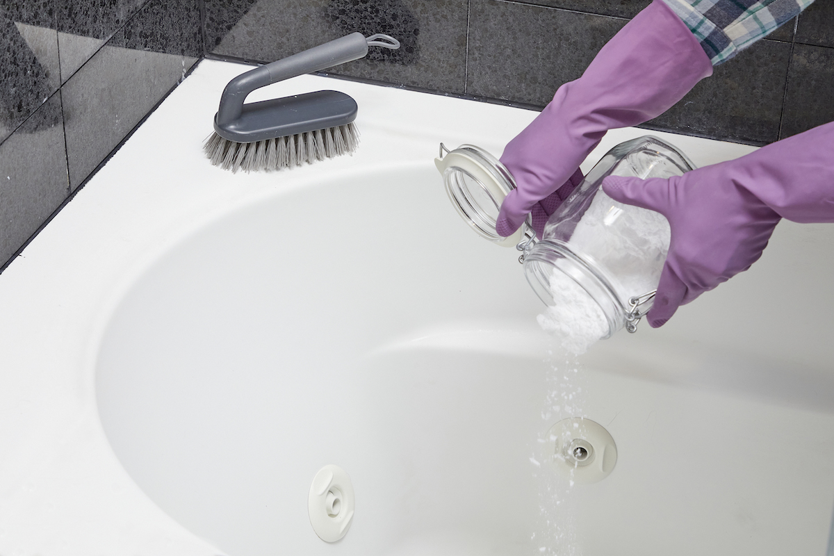 Woman sprinkles a baking soda mixture into the bottom of her bathtub.