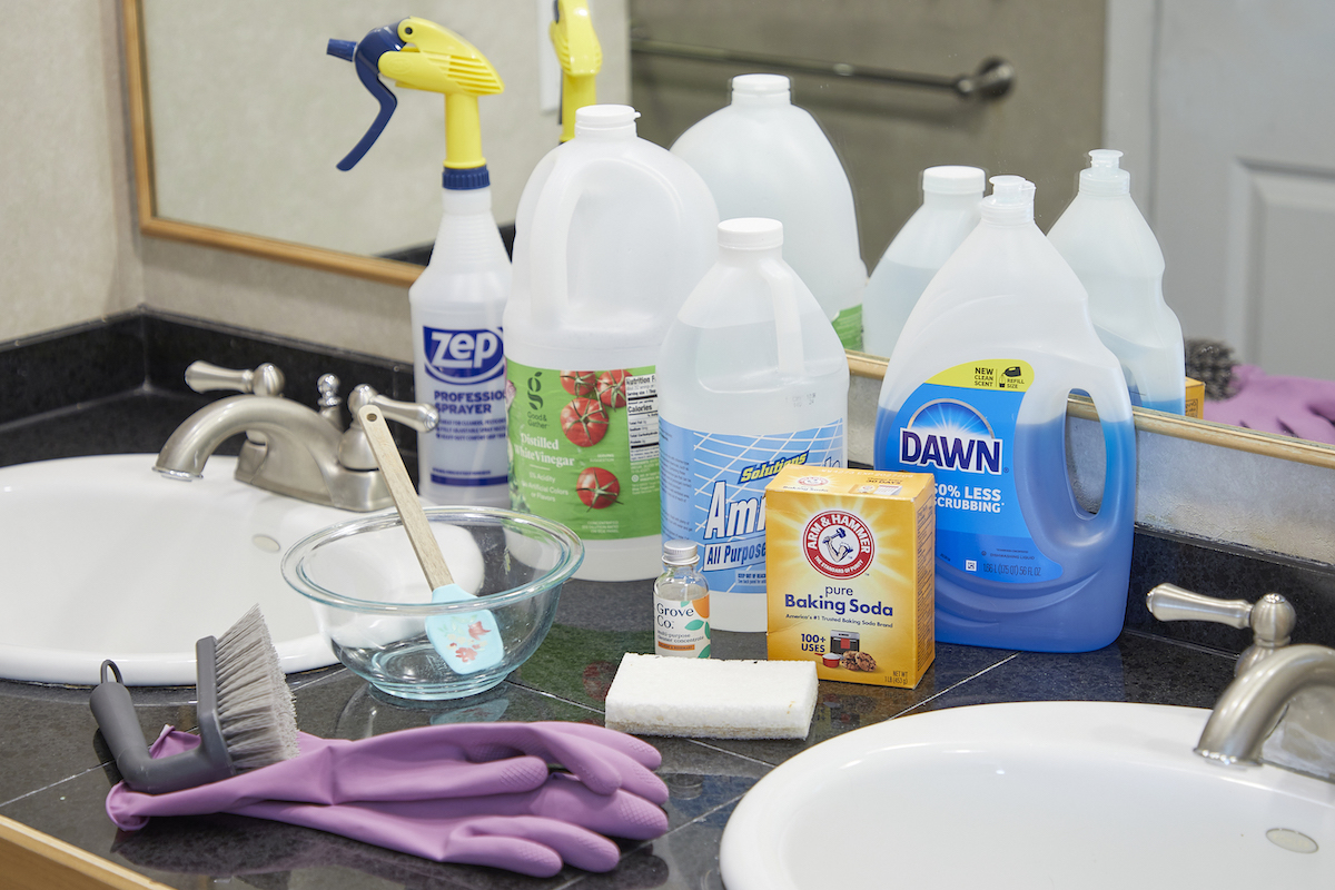 Bottles of ammonia, dish soap, vinegar, and other cleaning materials spread on a bathroom vanity.