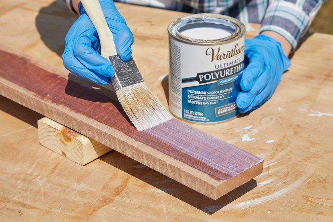 Woman uses a bristle paintbrush to apply polyurethane to a piece of wood.