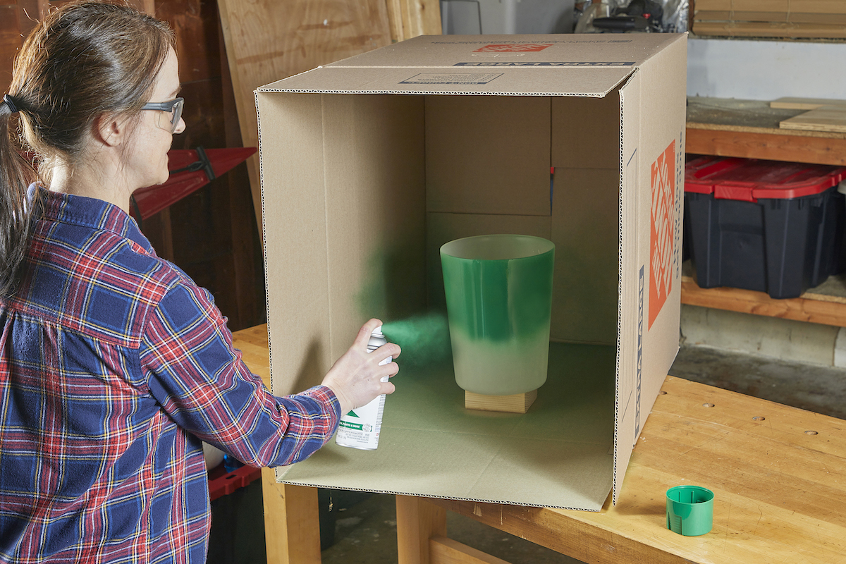 Person using spray paint to paint plastic bin green.