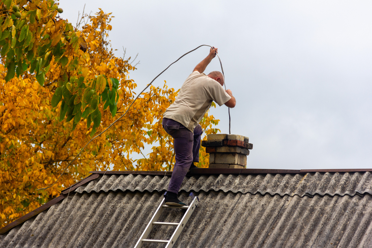 a male chimney sweep cleans the chimney from soot on the roof of a village house, preparation for the heating season