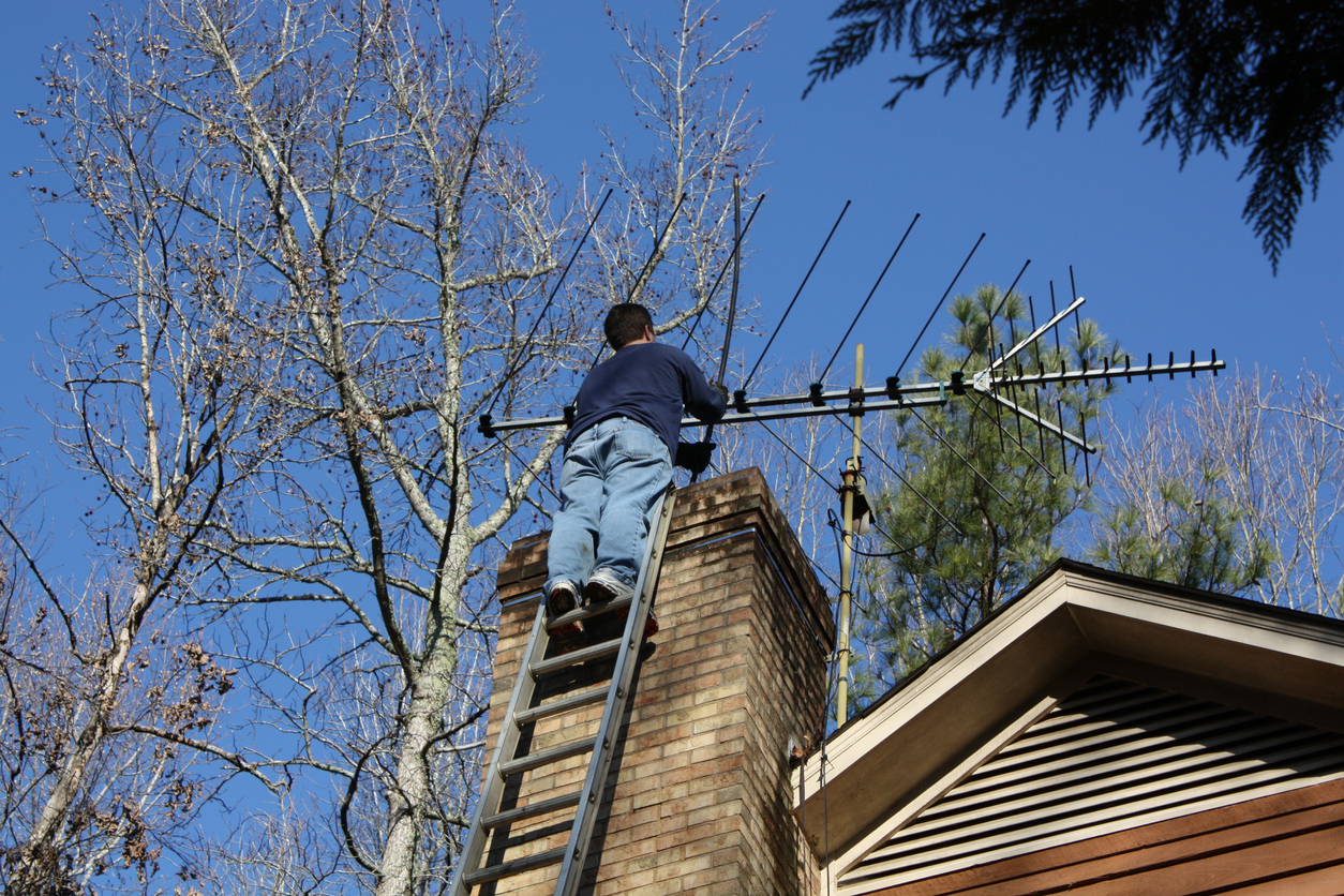 Man working, cleaning out chimney at top of house.