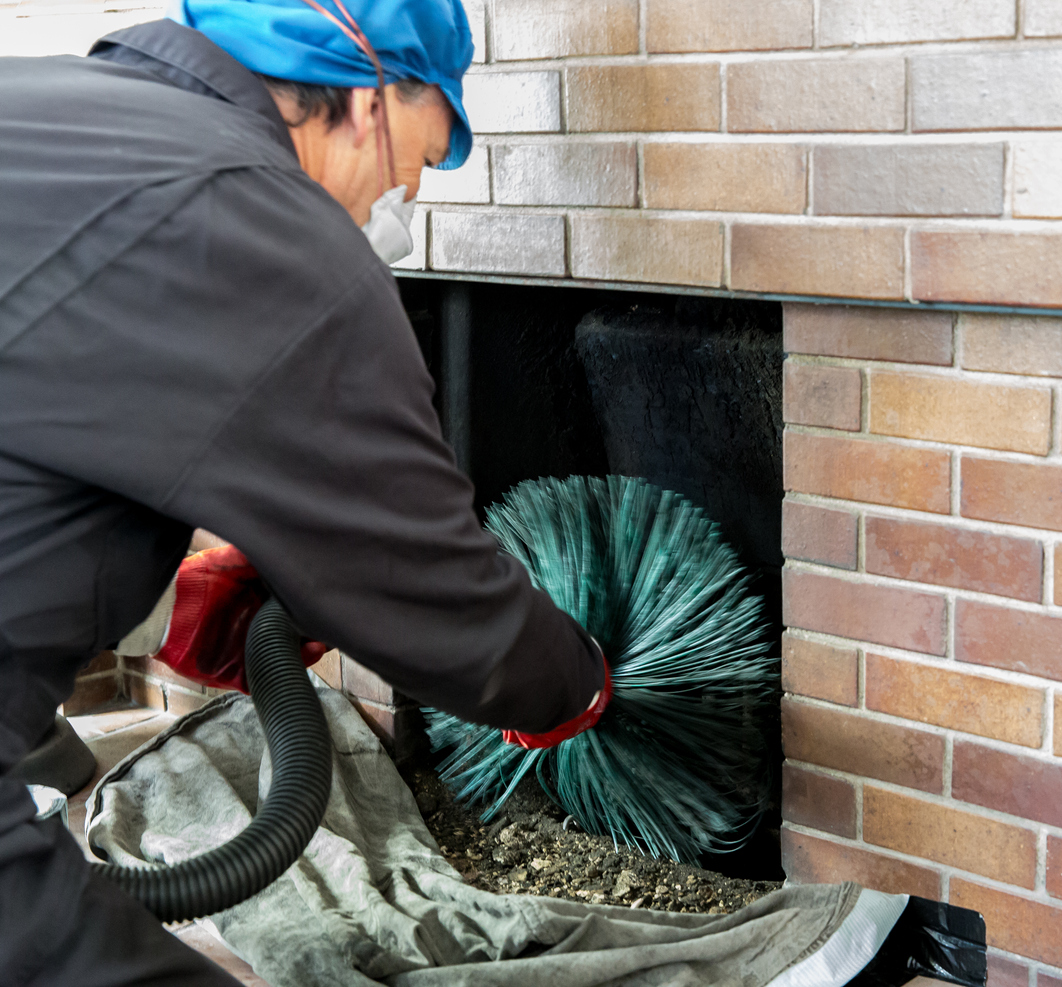 Chimney sweep wearing a mask for protection whilst cleaning chimney - screwing the chimney sweep brush as it ascends the chimney