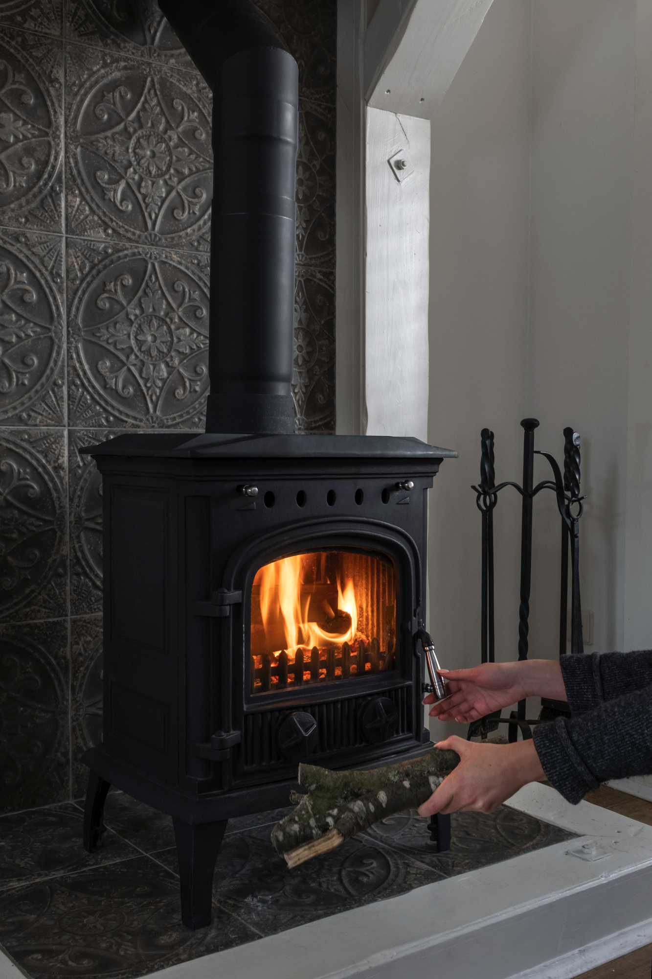 New wood stove in black metal with tall pipe against grey stone wall.