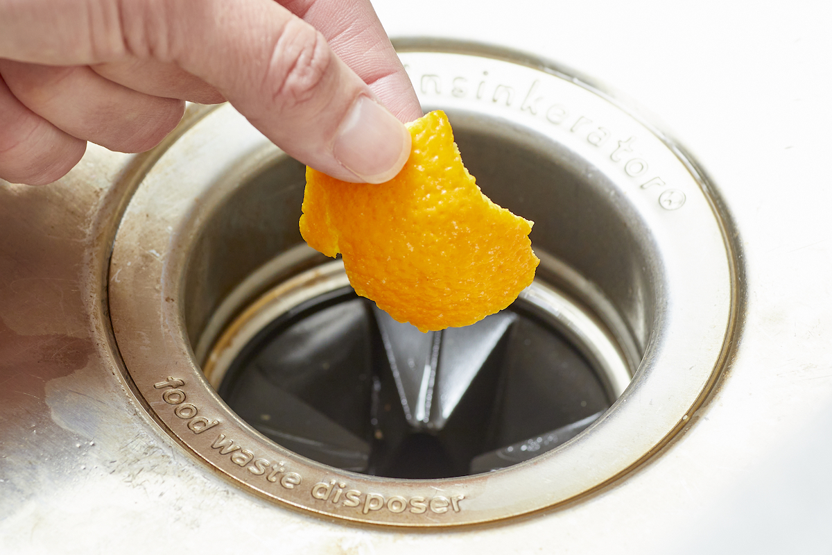 Person is about to drop an orange peel into a garbage disposal.