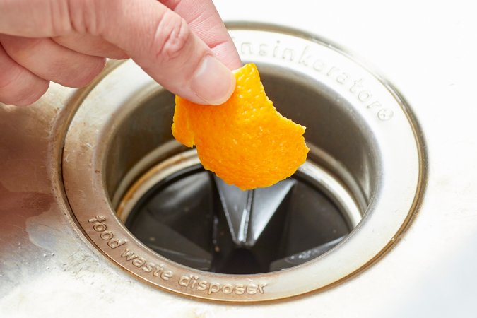 Person is about to drop an orange peel into a garbage disposal.