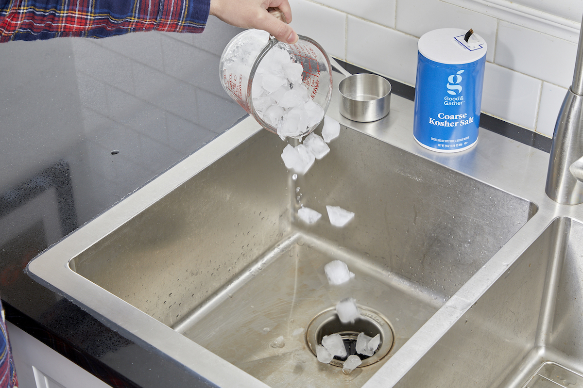 Woman dumps ice cubes into kitchen sink, a container of salt nearby.