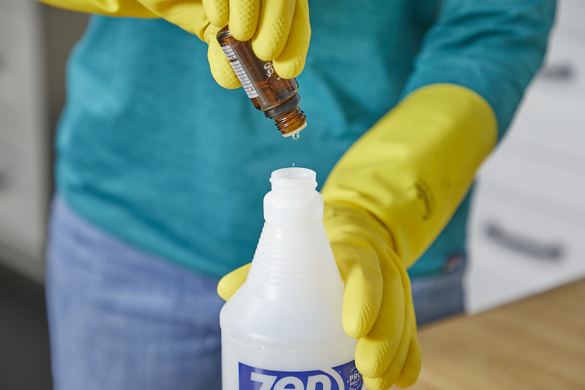 Woman wearing cooking gloves adds essential oil to a spray bottle.