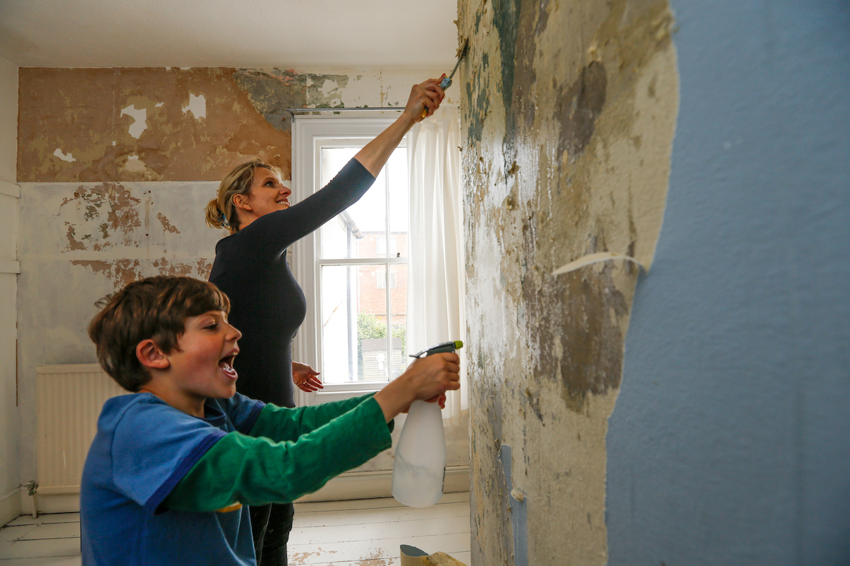 A mother and son scraping off old wallpaper and glue off a bedroom wall.