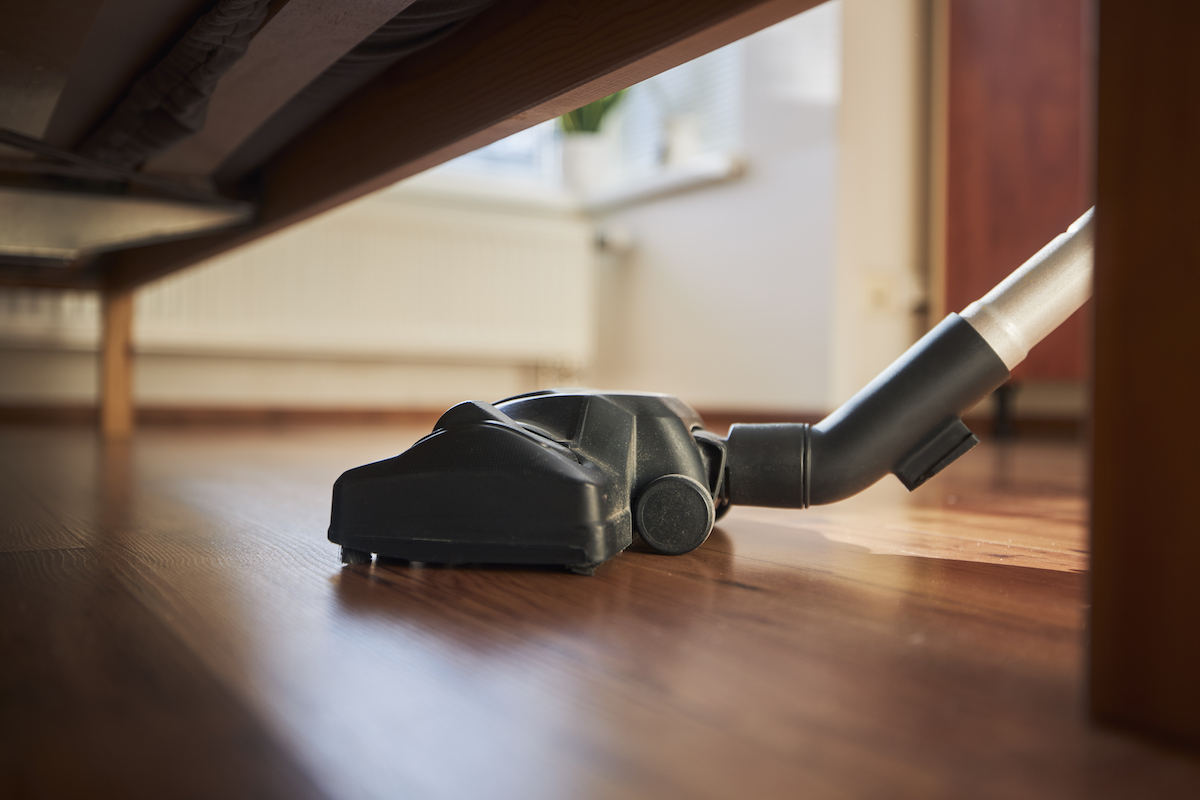 Close-up of vacuum cleaner cleaning a wood floor under a sofa.