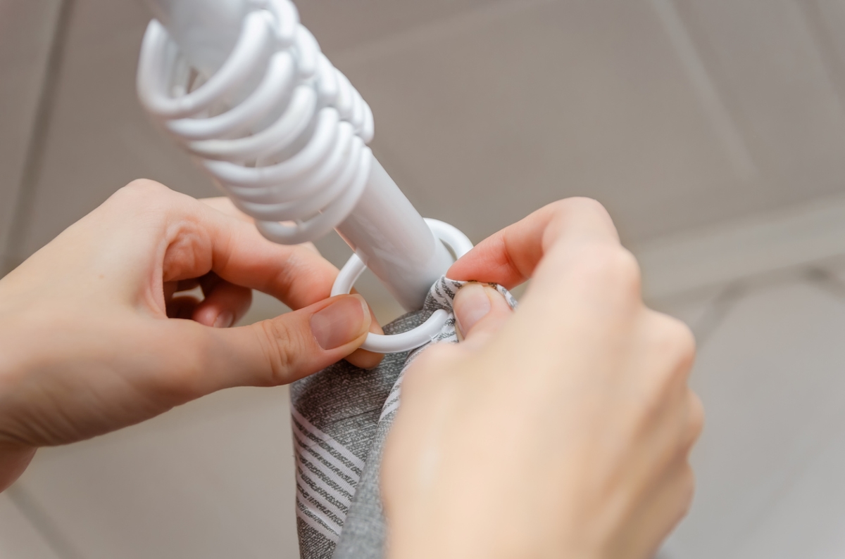 Person hands on shower curtain rings.