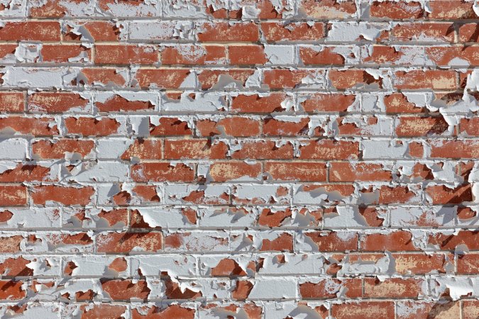 Peeling white paint on an old brick wall.