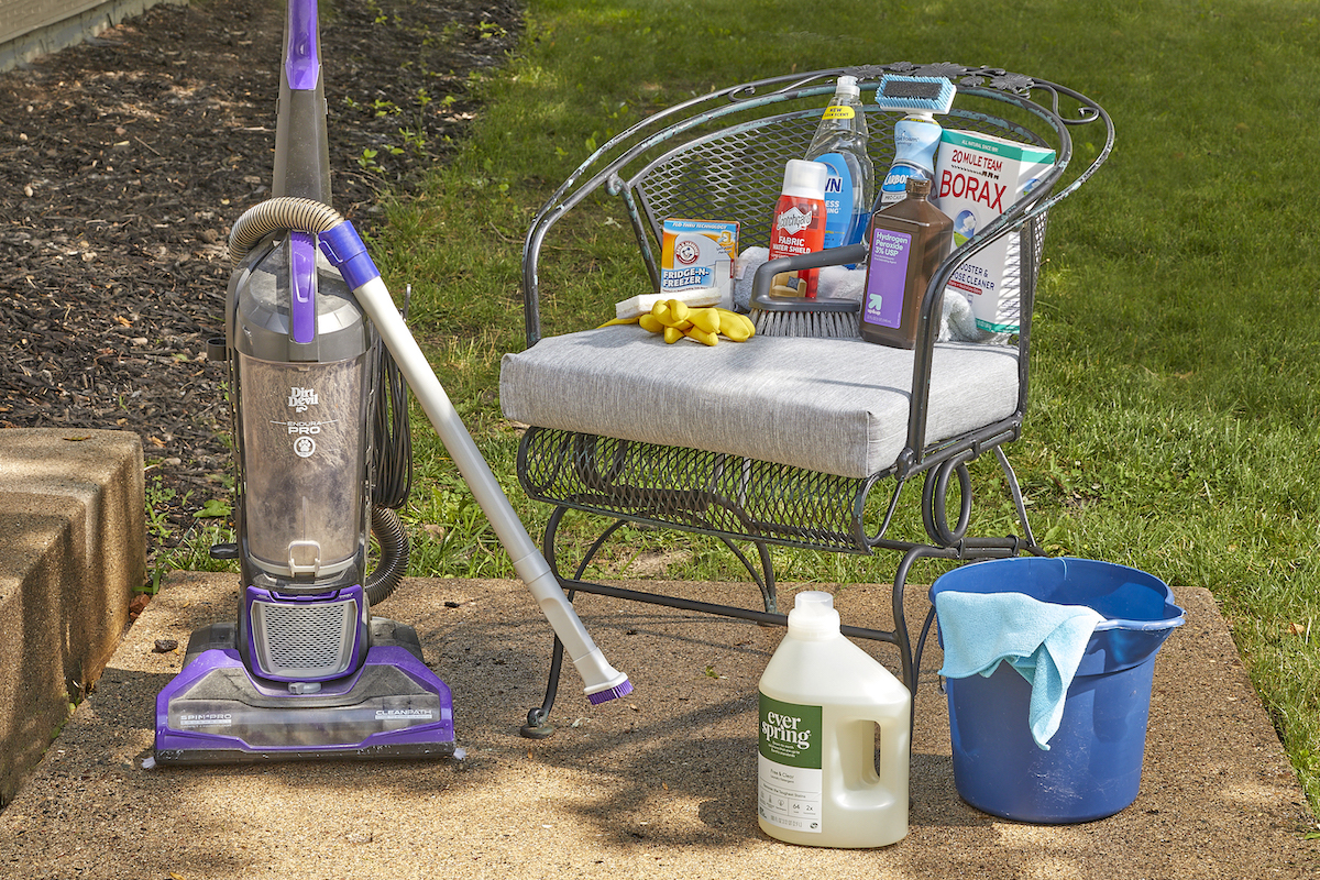 A patio chair with cushion surrounded by a vacuum cleaner and materials needed to clean the cushions.