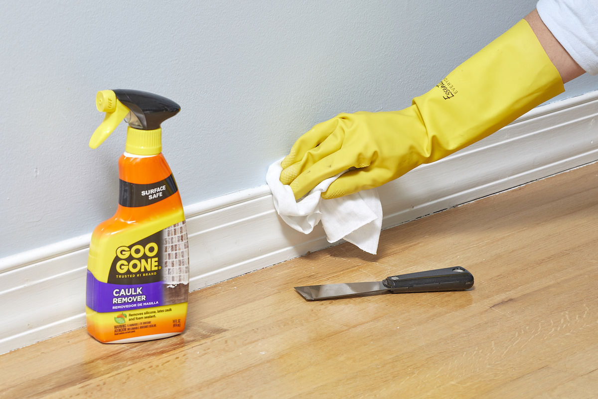 Woman sprays Goo-Gone onto baseboard caulking and wipes it with a cloth.