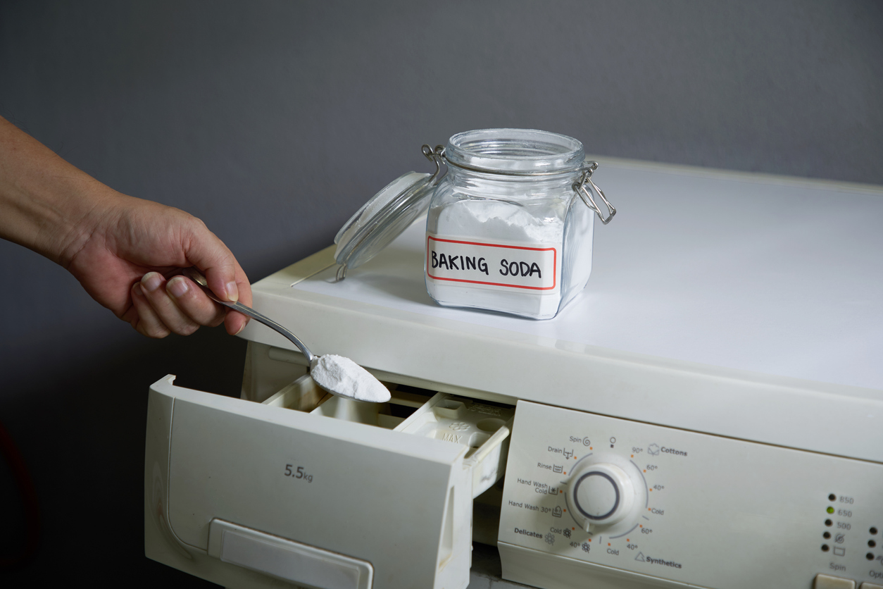 baking soda and vinegar hand dumping spoonful of baking soda into washing machine