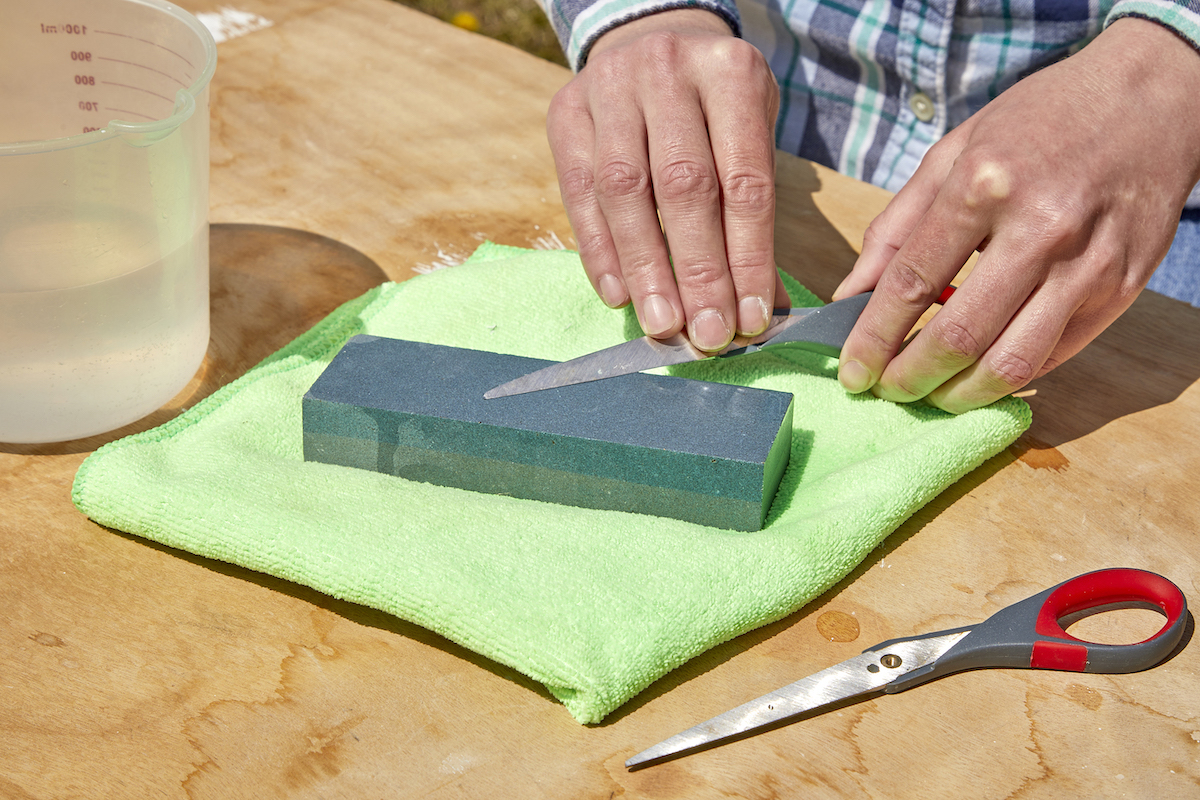 Woman uses sharpening stone to sharpen one blade of a scissor.