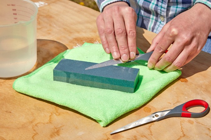 Woman uses sharpening stone to sharpen one blade of a scissor.