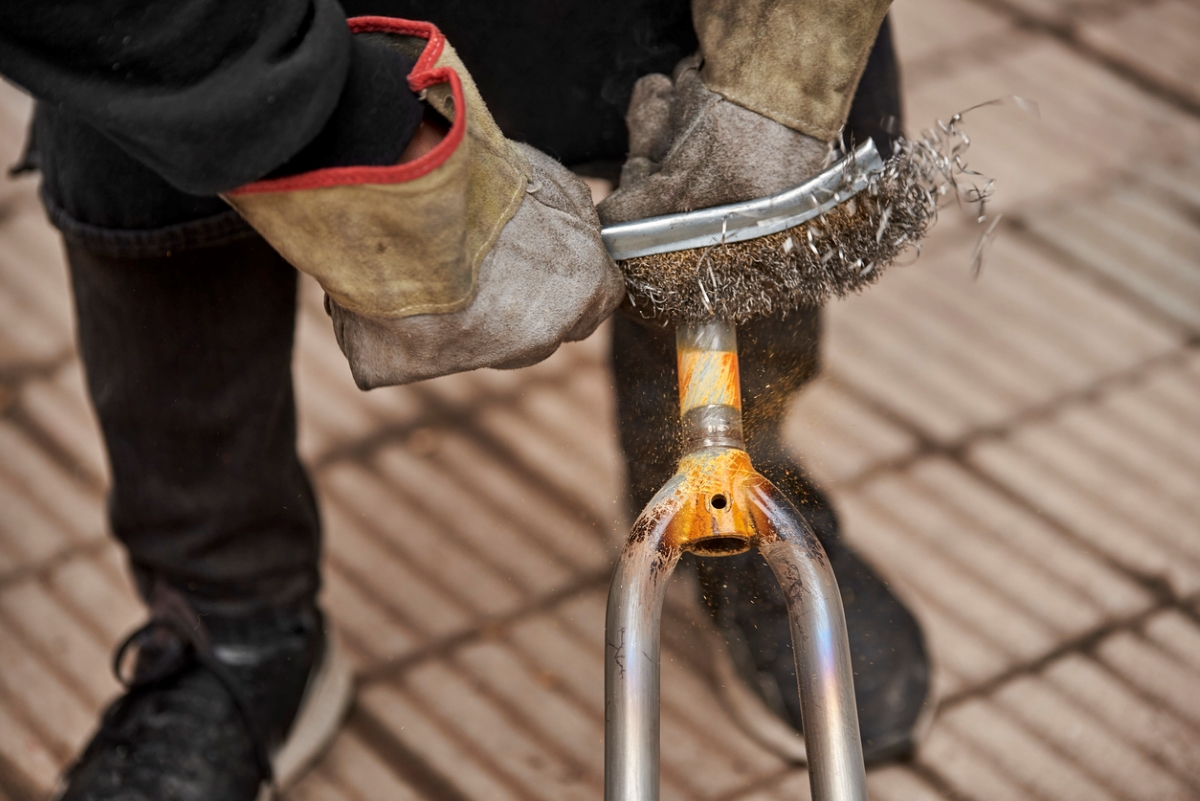 Person using wire brush to remove paint from metal.