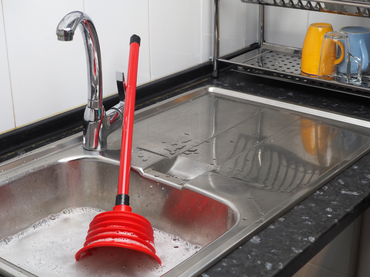 Clogged pipes in the kitchen. Sink full of dirty water, red plunger