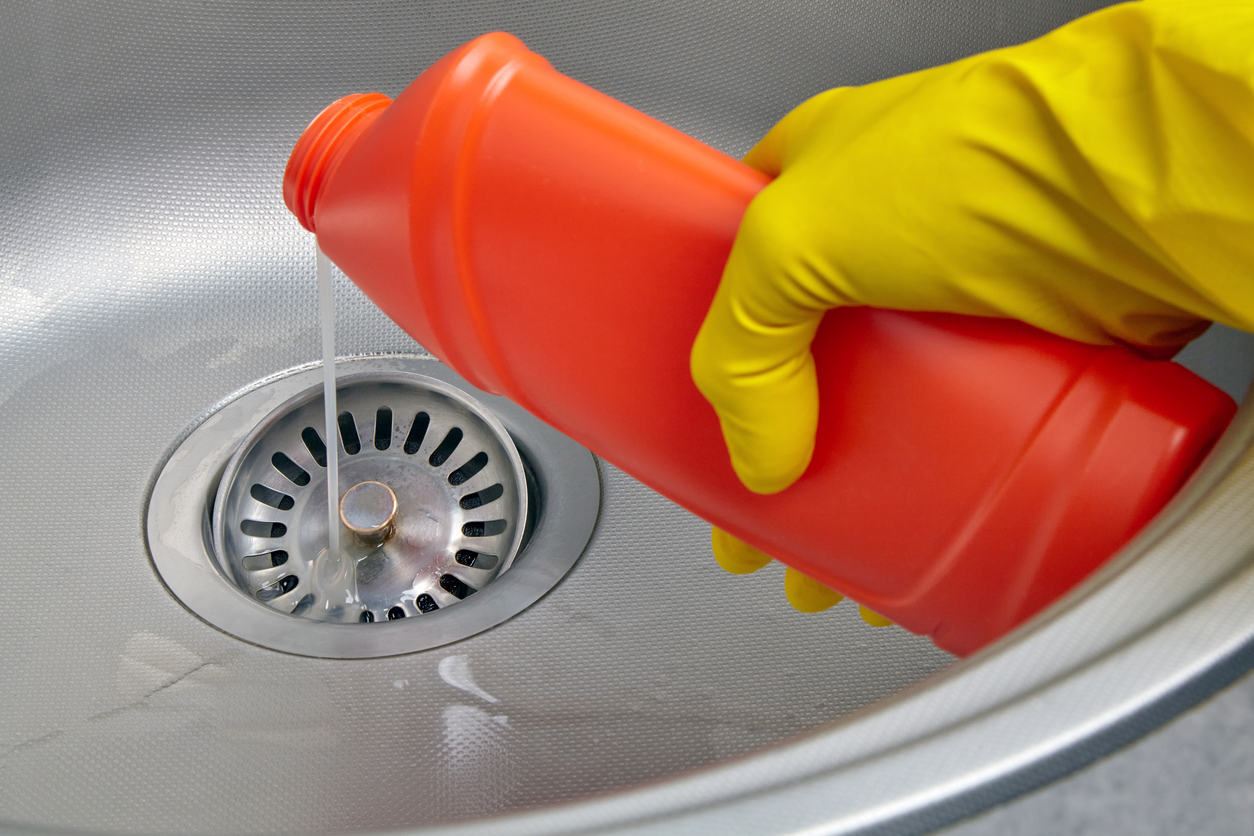 Hand in yellow rubber glove pour sewer pipe cleaner down the kitchen sink drain. Kitchen and drain cleaning work