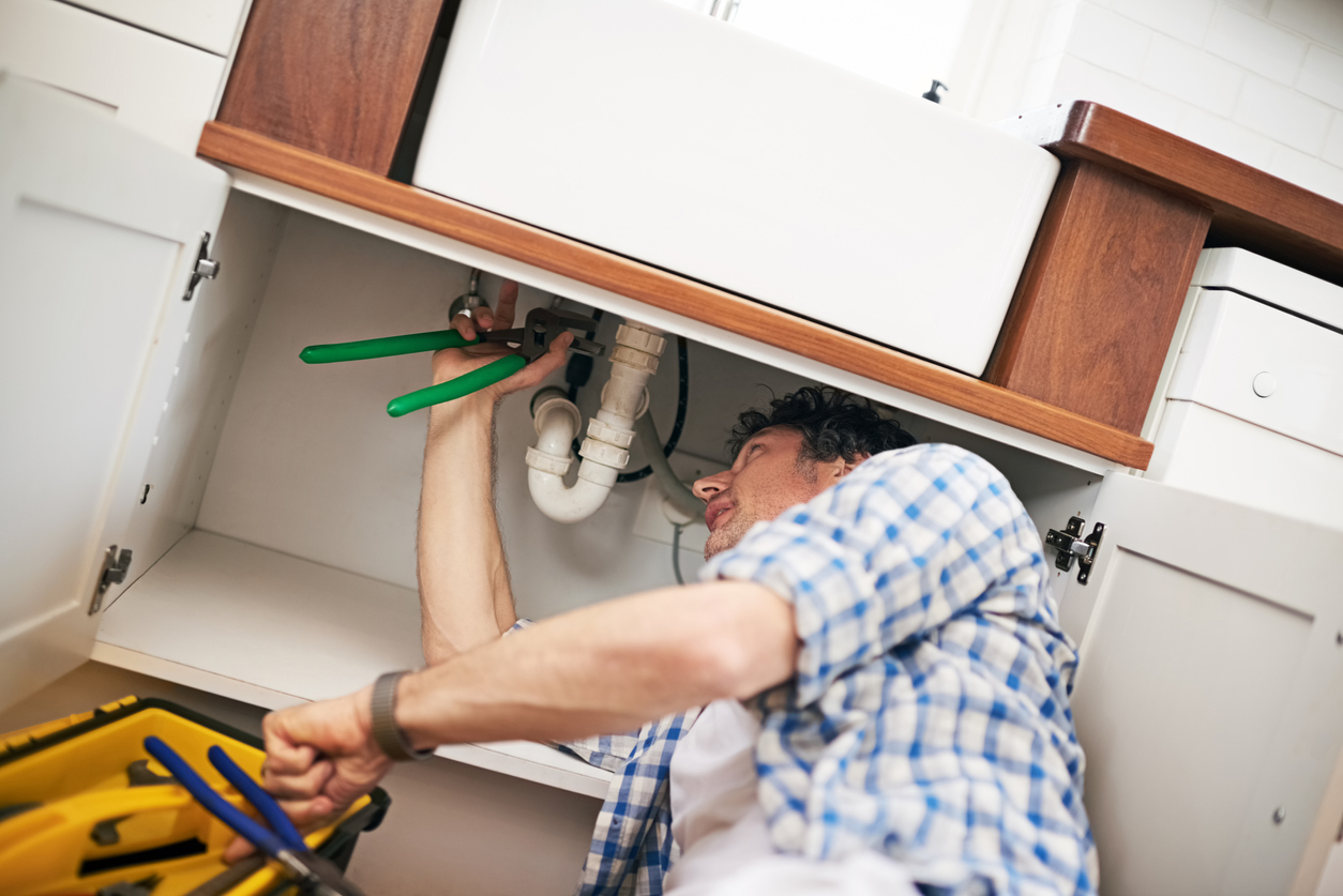 Shot of a man fixing a pipe under his kitchen sink