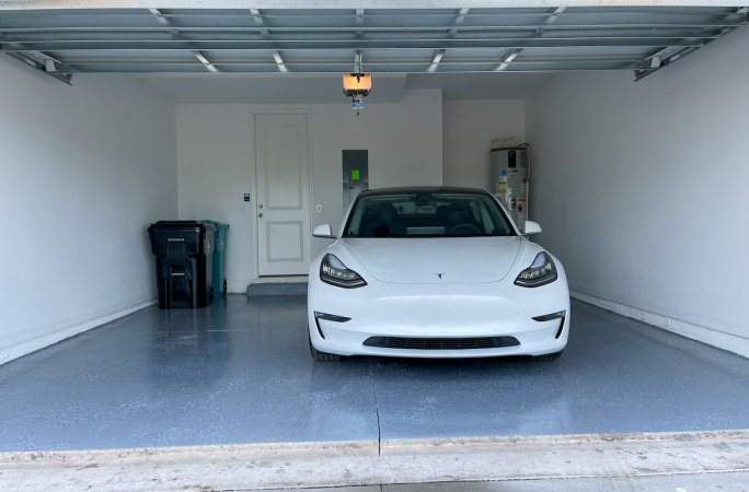 A freshly painted garage floor with a gray epoxy finish, a white sedan parked inside.