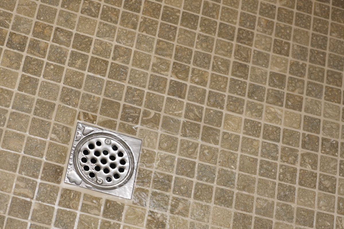 A drain at the bottom of a shower with beige tiles.