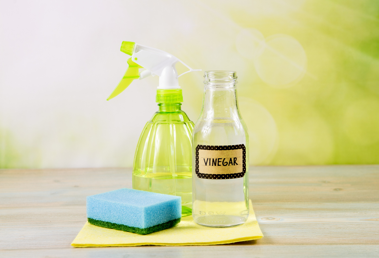 Chemical free home cleaner products concept. Using natural destilled white vinegar in spray bottle to remove stains. Tools on wooden table, green bokeh background, copy space.