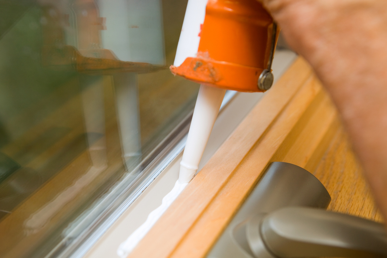 A person sealing a window gap with a caulking gun.