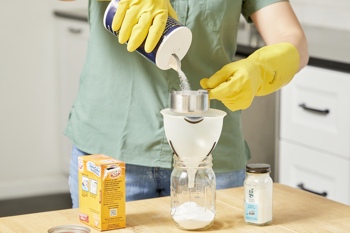 Woman wearing cleaning gloves pours salt through a funnel into a mason jar.