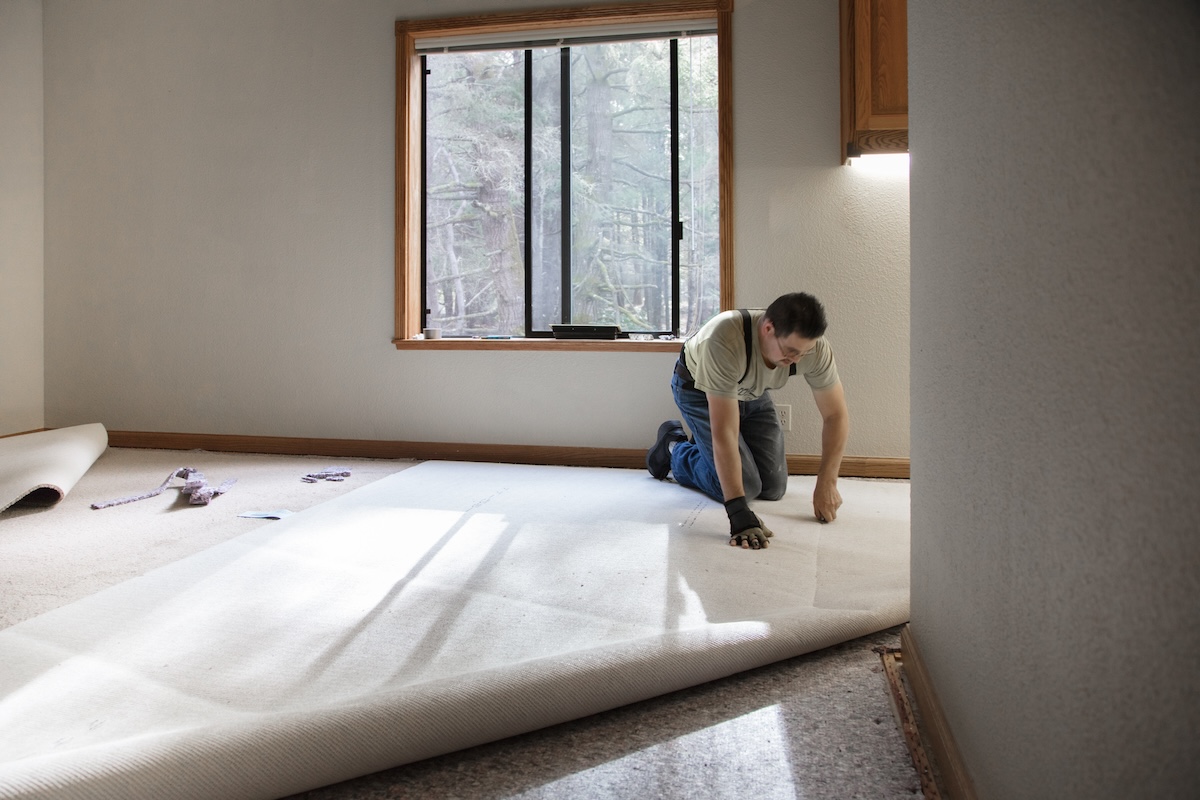 A profession installs carpet in a sunny room.