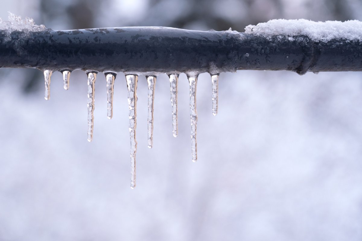 Metal pipe outdoors surrounded by snow, dripping with icicles.