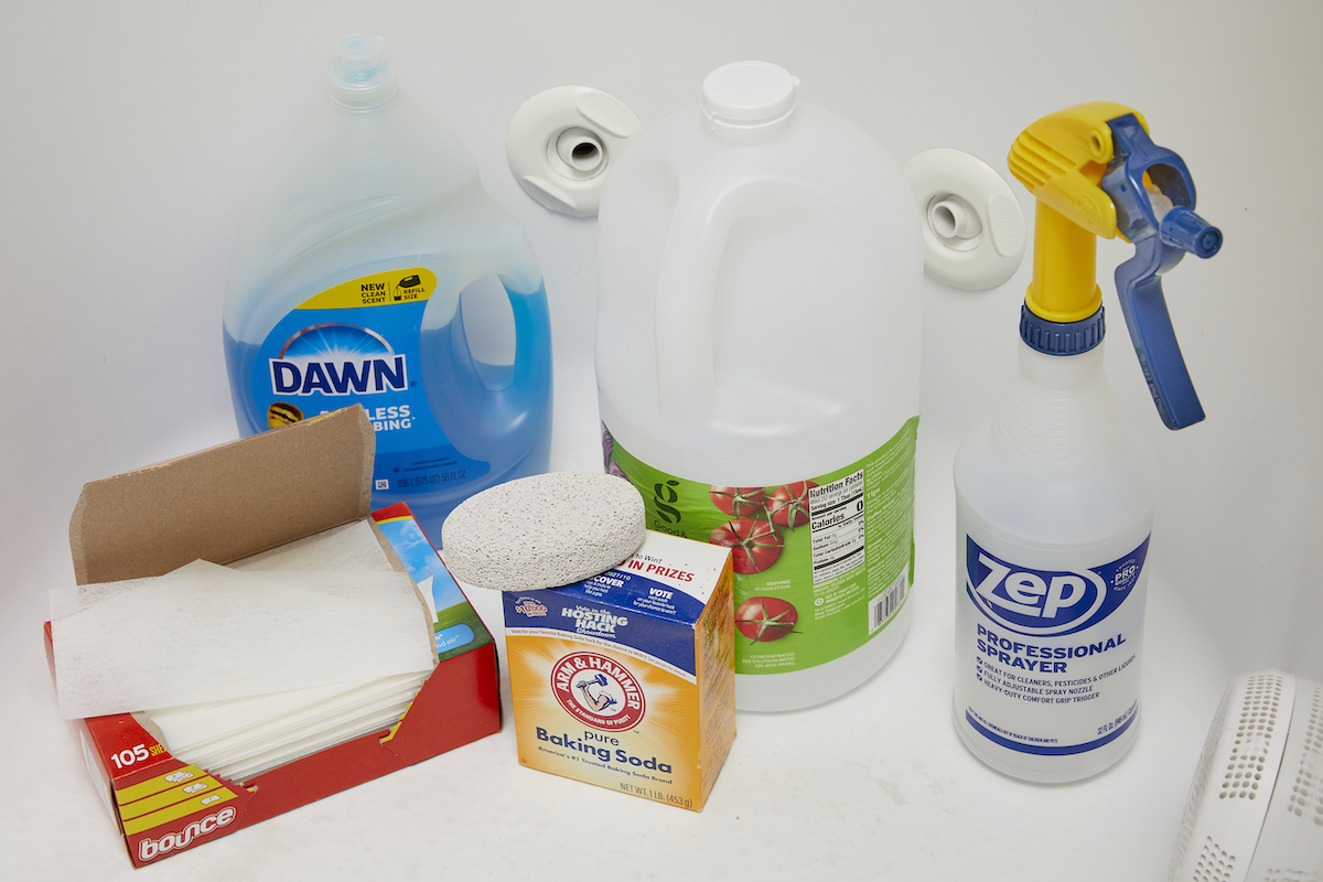 Some materials used to clean soap scum, including dish soap, vinegar, and dryer sheets—all inside a bathtub.