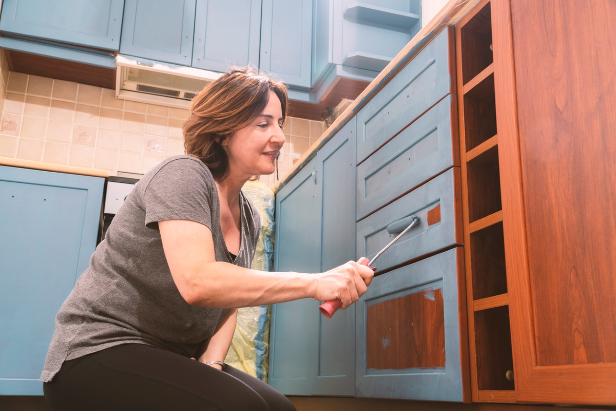 Woman using roller to paint laminate cabinets teal