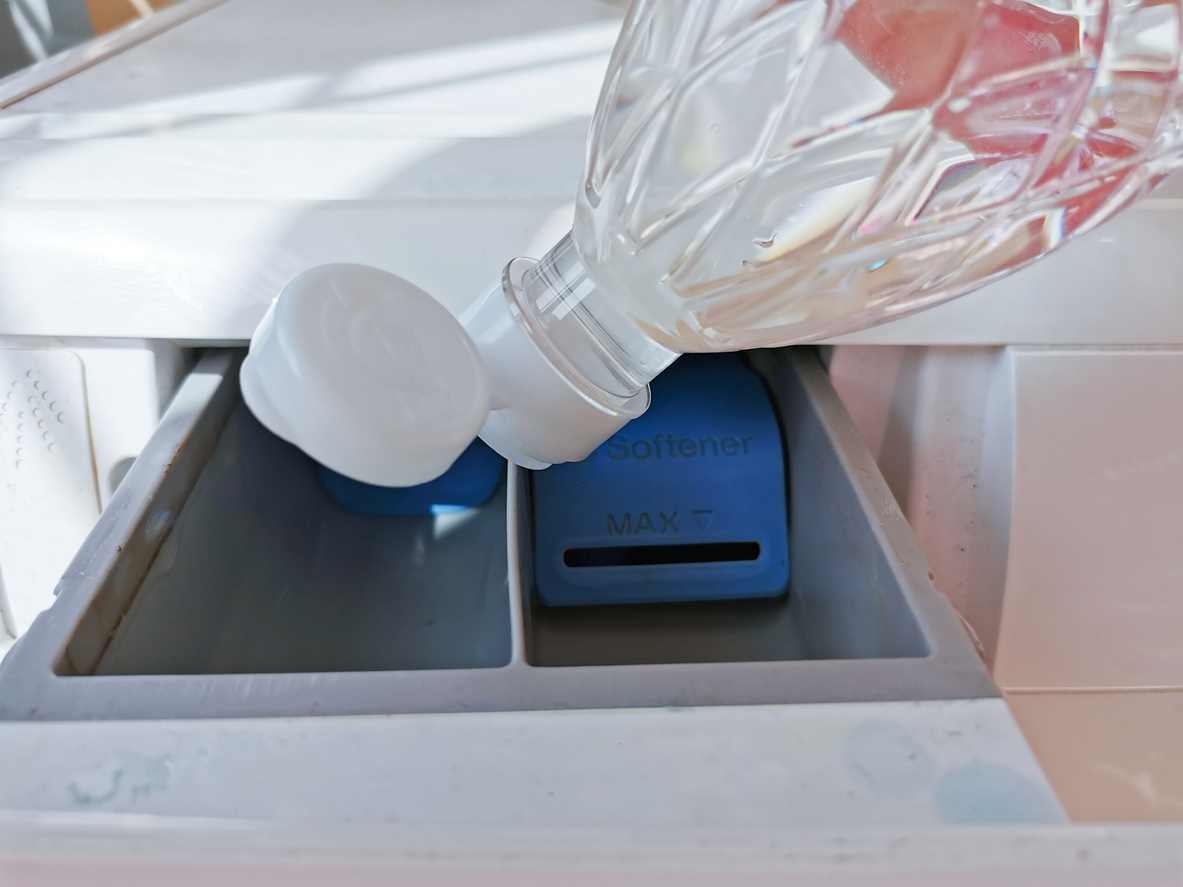 A person is pouring vinegar into the dispenser tray of a washing machine.