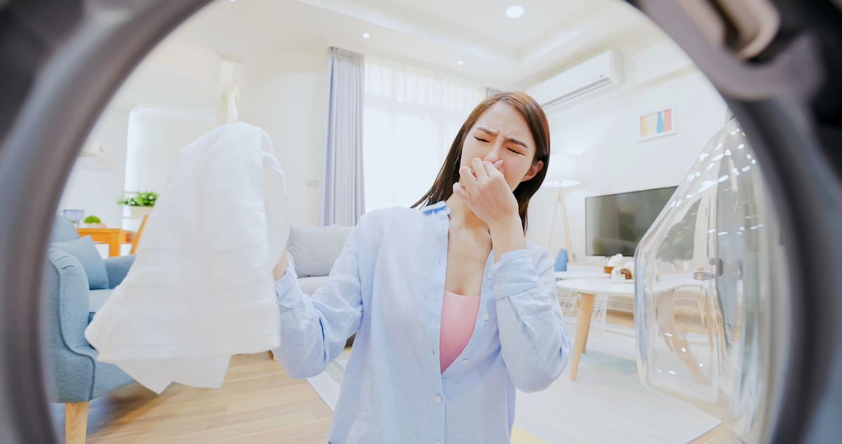 A woman is disgusted with the smell of the clothing she has removed from the washing machine.