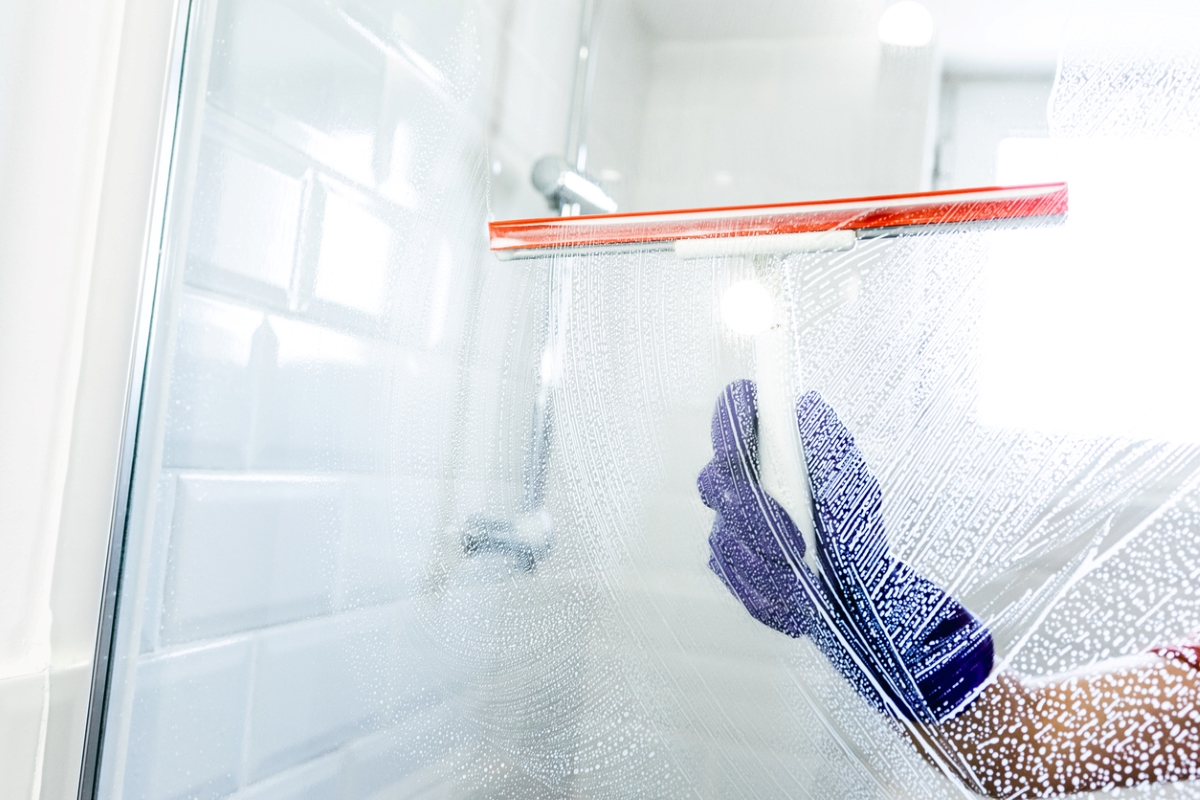 Person using a squeegee on shower glass in the bathroom.