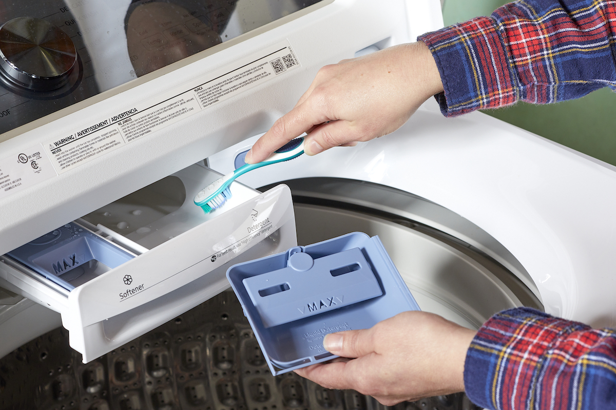 Woman takes detergent dispensers in washing machine apart and scrubs with toothbrush.